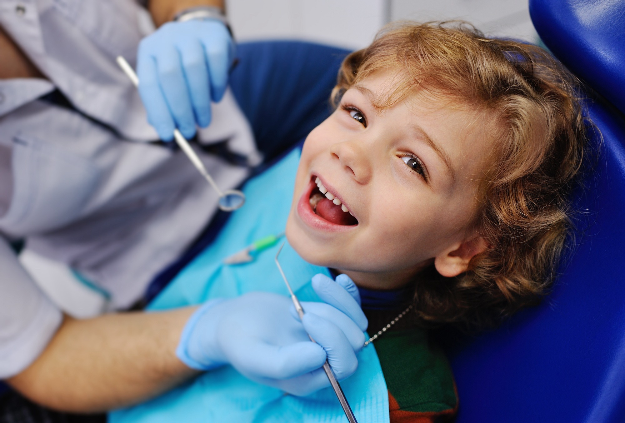 smiling child sitting in a blue chair dental
